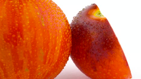 disparo macro de un tomate a rayas de globo rojo entero y una mitad de tomate rosa índigo girando lentamente en la mesa giratoria aislada sobre el fondo blanco.
