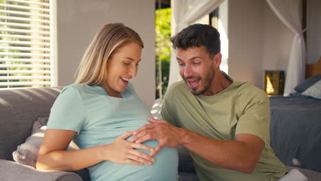 couple with pregnant woman in bedroom at home with man feeling baby kicking