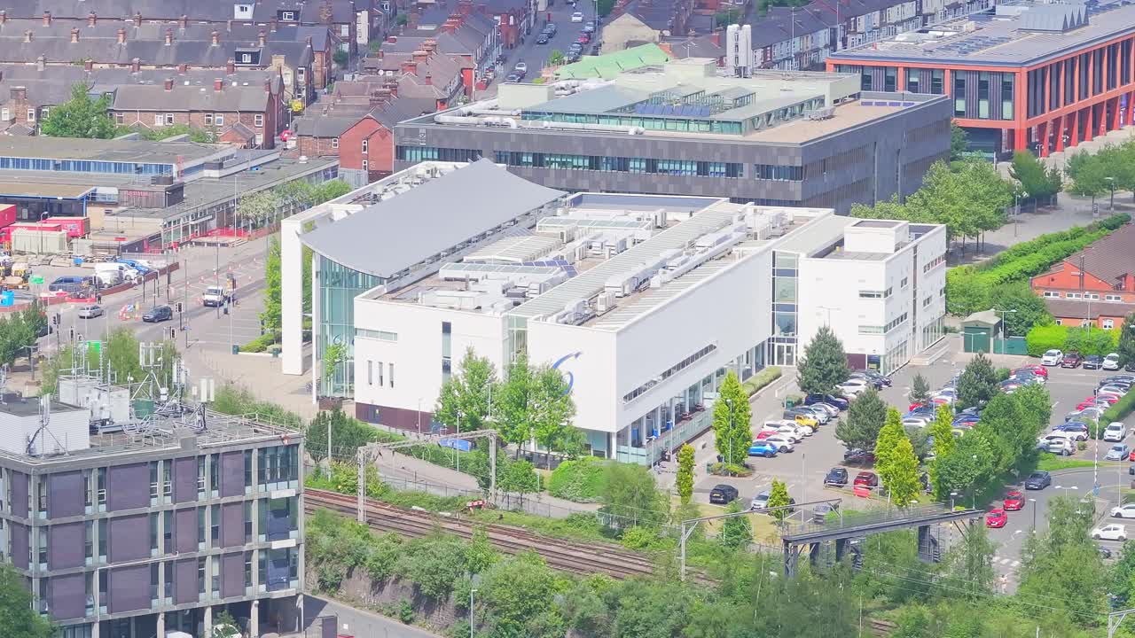 Stoke-on-Trent showing the Cauldon Campus of Stoke-on-Trent College, with its modern curved-roof building surrounded by trees, parked cars, and adjacent red-brick and grey structure