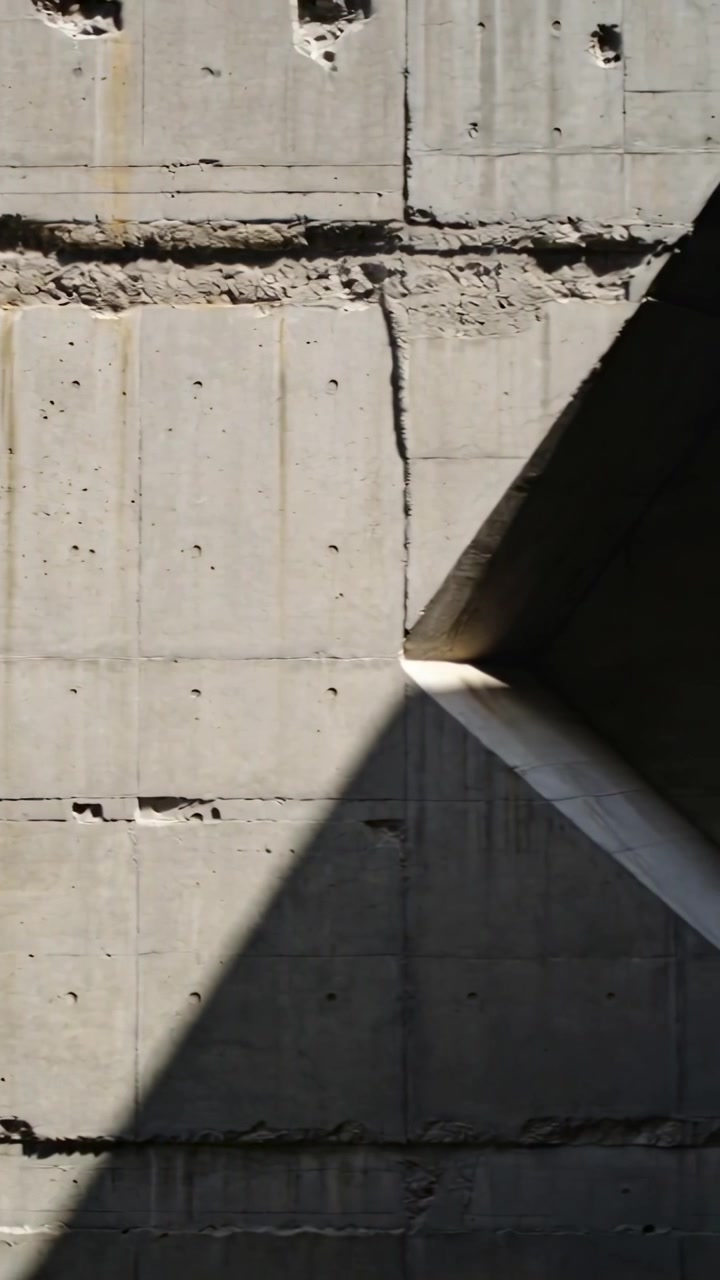 Video vertical: Cámara panorámica revelando un hueco triangular y una sombra en una pared de hormigón para mostrar las juntas.