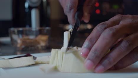 Young-black-man-dicing-fresh-ripe-peeled-eggplant-on-plastic-cutting-board