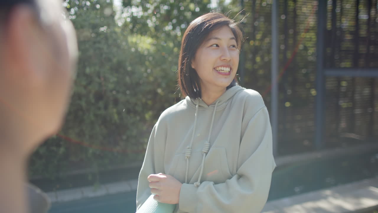 행복한 아시아 여성 친구들이 운동 매트와 물 병을 가지고 테라스에서 이야기하고, 느린 동작