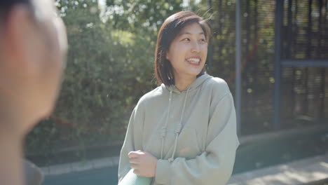 Happy-asian-female-friends-with-exercise-mat-and-water-bottle-discussing-on-terrace,-slow-motion