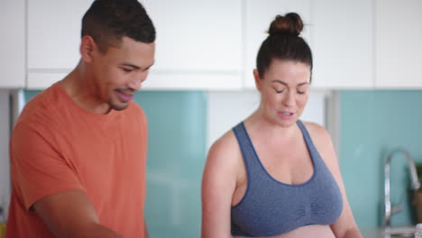 smiling pregnant woman and partner preparing healthy meal in modern kitchen