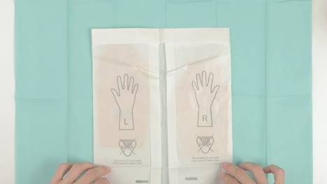 primer plano del personal sanitario abriendo y extendiendo un paquete de guantes quirúrgicos estériles en un paño