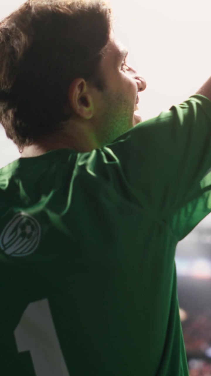 Video verticale. Vista posteriore di un portiere che saluta i tifosi ed entra nello stadio con il pallone sotto il braccio.