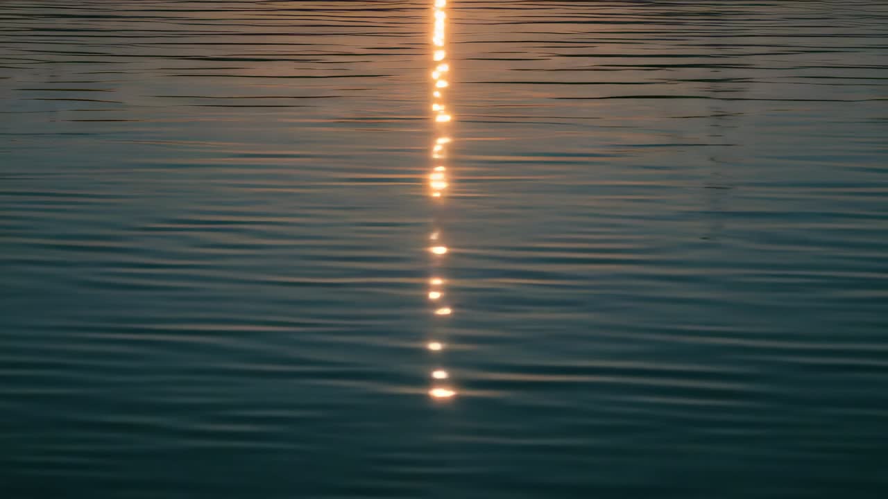 Shimmering sunlight column splitting into bright beads on calm water with ripples from low sun
