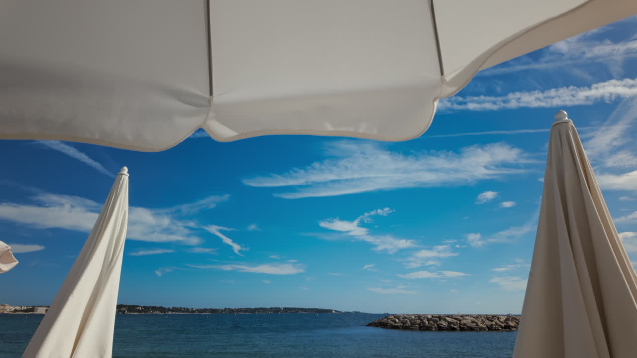 Sunny seaside view with white beach umbrellas framing a bright blue sky and calm sea