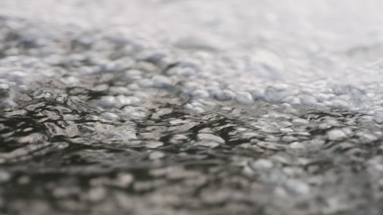 Detailed close-up of a bubbling water surface, capturing dynamic ripples and textures for a calming and natural scene. Slow Motion.