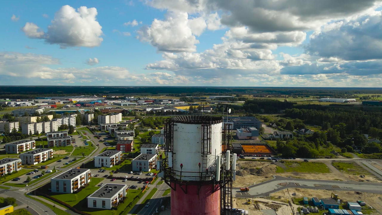 Aerial drone video flying around a tall smoke stack chimney tower that has 5G and 6G electronic transmittors and radio equipment on it during a sunny day in a small city area at summer time.