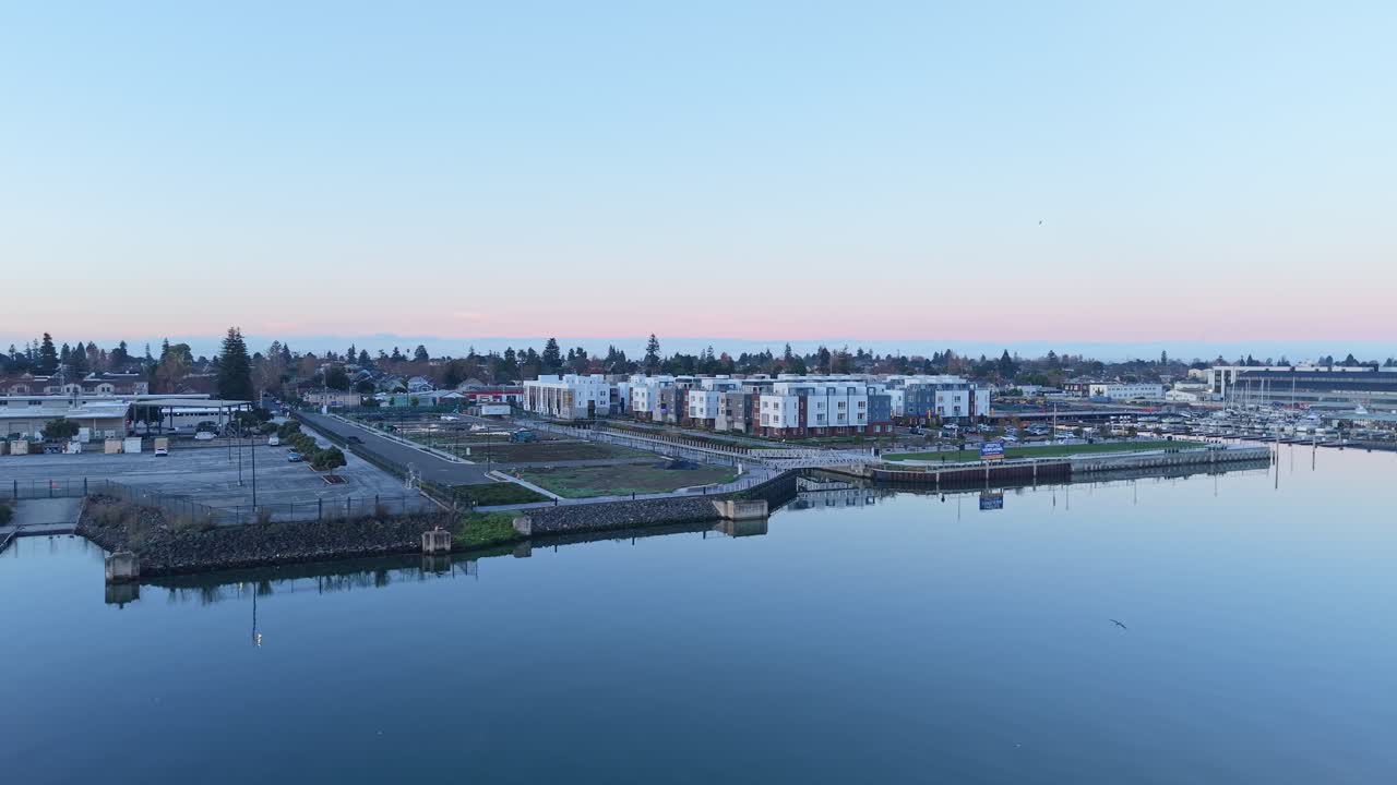 I colori tenui dell'alba illuminano il Svendsen Maritime Park dall'alto, mentre il filmato aereo cattura la tranquillità dei moli, l'acqua calma e i cieli stratificati che definiscono il fascino costiero di Alameda