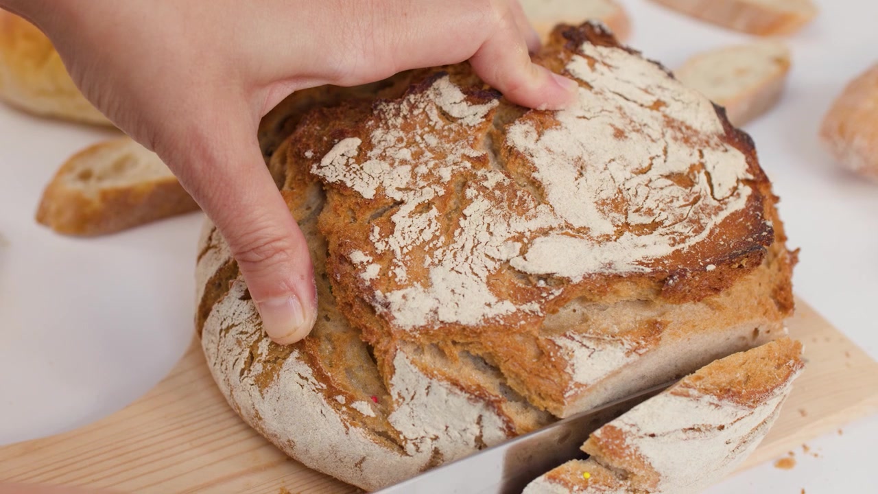 Primo piano di mani che affettano pane artigianale a lievitazione naturale con un coltello su sfondo bianco
