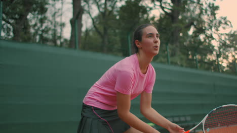 young tennis player backhand. young girl in pink t-shirt playing lawn tennis at sunset. eye level