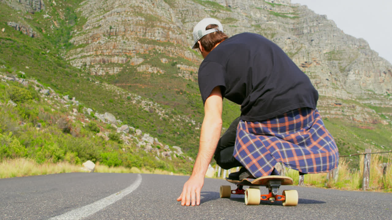 vista trasera de un joven fresco montando en patineta cuesta abajo en la carretera de campo 4k
