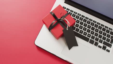 portátil y caja de regalo roja con cinta negra y etiqueta de regalo, sobre fondo rojo con espacio para copiar