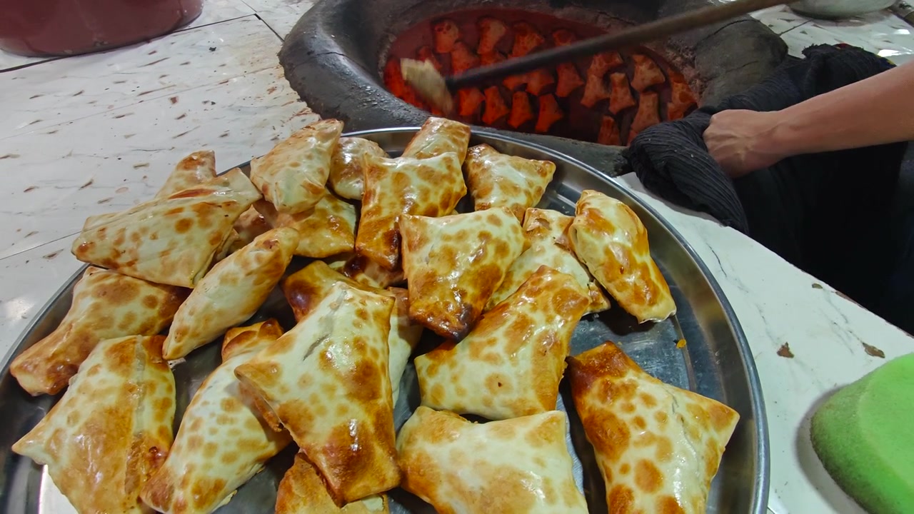 Fornaio che rimuove samsa appena sfornati da un tradizionale forno tandoor