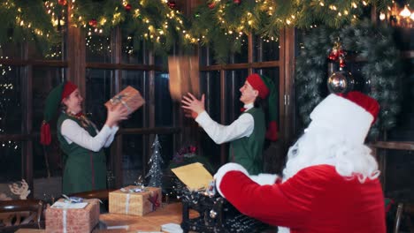 santa claus sitting at a table in a decorated room typing on an old typewriter. elves play with gift boxes. new year's residence santa claus