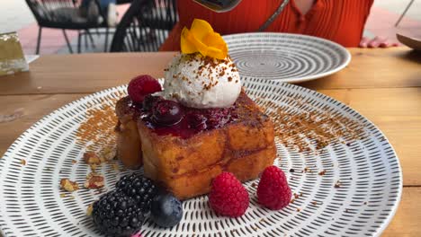 pouring maple syrup over delicious french toast with forest berries, cinnamon, coconut cream ball and nuts, sweet breakfast, traditional french dish, 4k shot