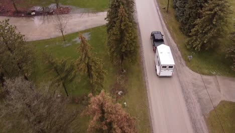 Camioneta-Negra-Remolcando-Un-Remolque-De-Caballos-A-Través-De-Una-Pequeña-Ciudad,-Vista-Aérea-De-Seguimiento