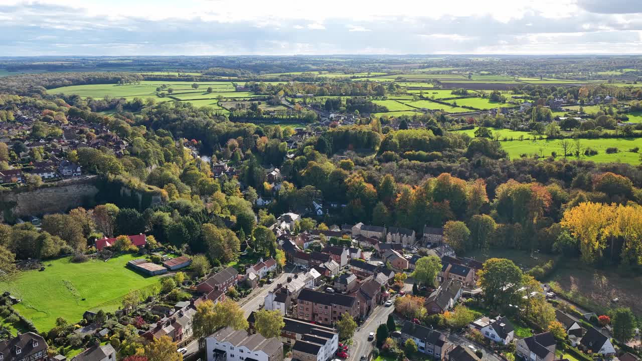 High angle drone descent shows clustered houses, tree-lined streets and the surrounding patchwork of cultivated fields, hedgerows and rolling countryside around Knaresborough, North Yorkshire, England
