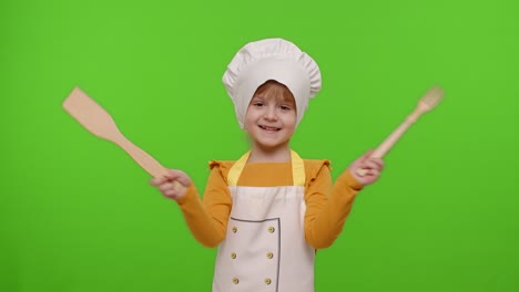 niña vestida con un delantal como chef cocinero bailando con tenedor y espátula en fondo de llave cromada