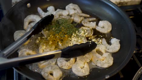 Shrimp-frying-in-a-pan-on-a-hot-stove-with-spices-and-herbs-mixed-in-and-steam-rising