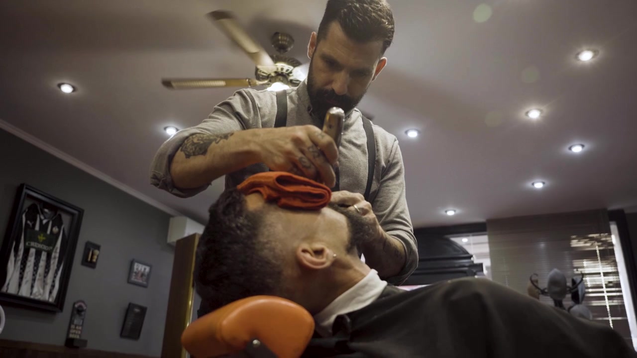 Barbeiro barbeando a barba de um cliente em uma barbearia - close-up