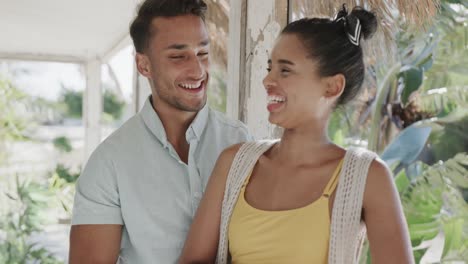 happy diverse couple talking and smiling on sunny beach house porch, in slow motion