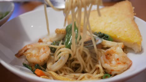 twisting some seafood spaghetti using a fork, which is served on a platter filled with pasta, seafood, and some spices