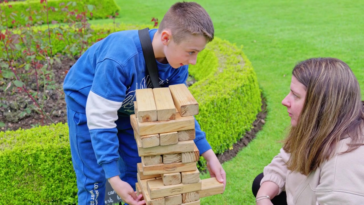 Un bambino e sua madre giocano a un gioco di costruzioni con blocchi di legno, ambientato in un giardino di campagna all'aperto