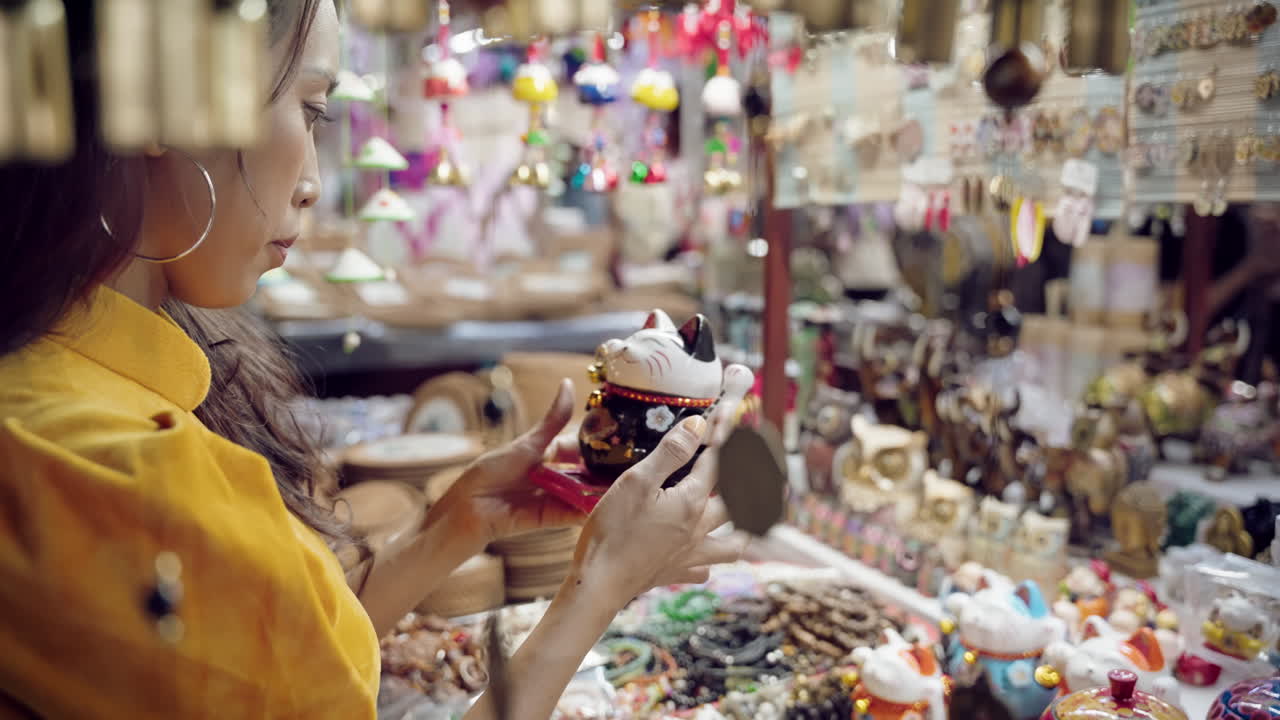 Woman in yellow Ao Dai examines handicrafts in Hoi An market, Vietnam, shallow focus