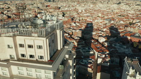 Aufsteigende-Aufnahmen-Des-Hochhauses-Torre-De-Madrid-Mit-Langem-Schatten-Auf-Den-Häusern-Unten.-Aufs-Dach-Kippen.