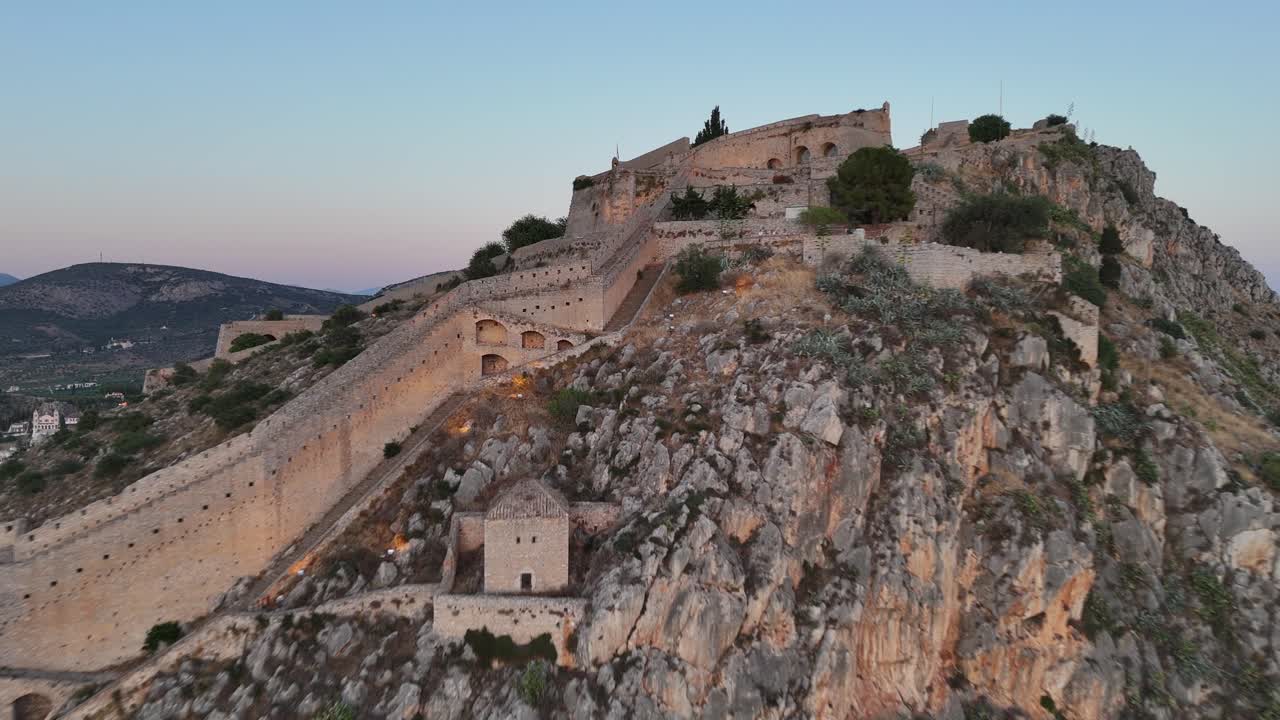 Peloponneso, Nauplia, vista aerea in avanti e panoramica a sinistra verso la fortezza di Palamidi, splendidamente illuminata durante il tramonto. Cielo rosa e blu, paesaggio stupendo.