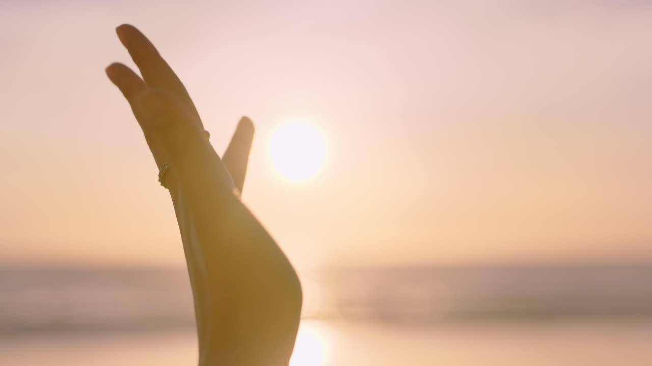 cerca de la mano de la mujer alcanzando la luz del sol en la playa jugando con los rayos dorados al atardecer