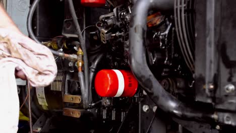 adult male caucasian technician hand checks oil on diesel generator by pulling grease dipstick, wiping with white rag and replacing, static close up profile