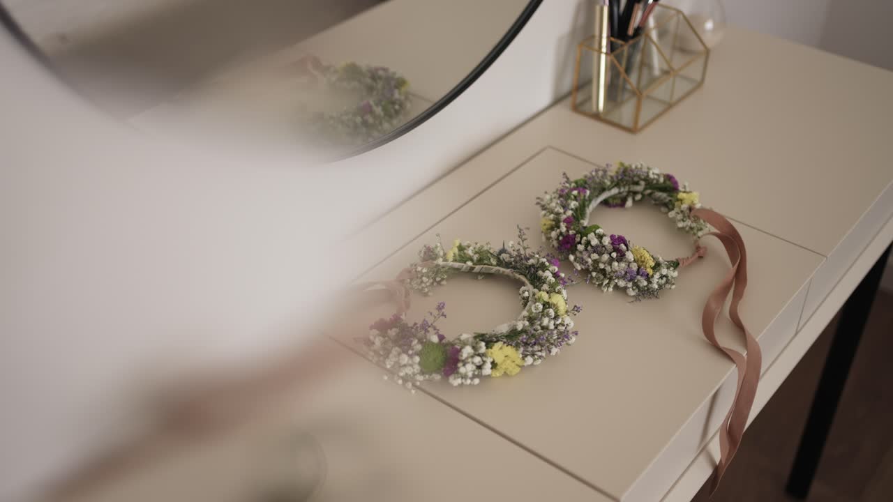 Two floral crowns with ribbons rest on a vanity, crafted with colorful blossoms and greenery