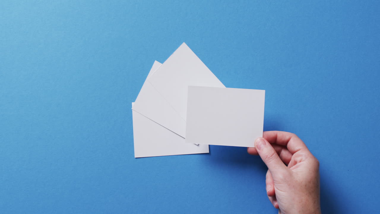 mano sosteniendo un pedazo de papel sobre pedazos de papel con espacio de copia en fondo azul en cámara lenta