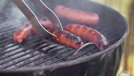 slow motion of tongs picking up a gristly sausage from smokey bbq grill