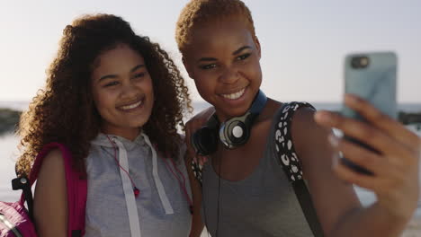 two friends using phone posing for selfie having fun on sunny beach