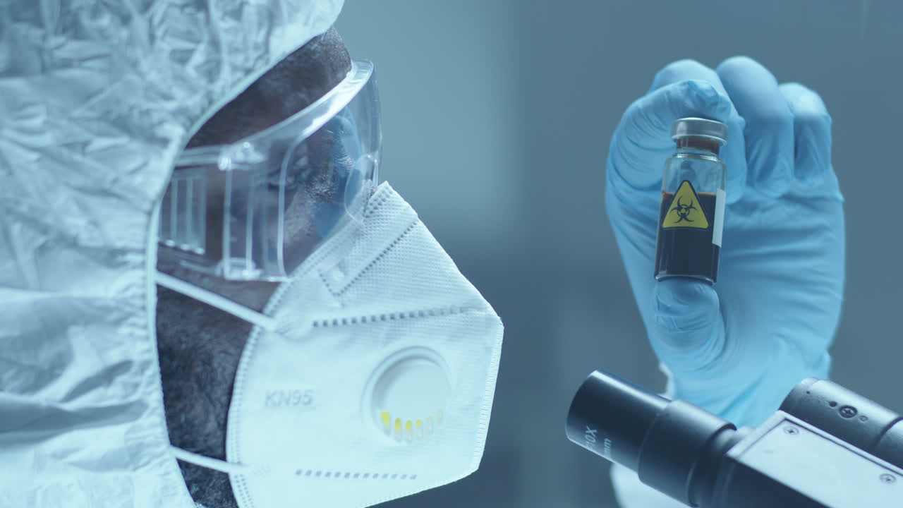 Lab Worker in Protective Overall and Mask Examining Blood in Test Tube