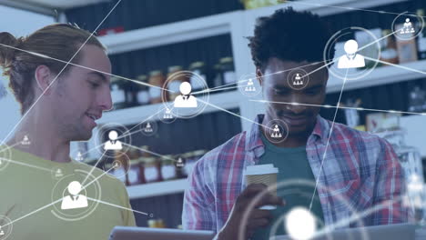 animation of network of profile icons over two diverse women discussing over a laptop at a cafe