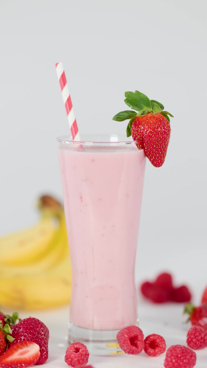Batido rosa cremoso en vaso alto, pajita a rayas, guarnición de fresa, iluminación de estudio brillante, toma estática