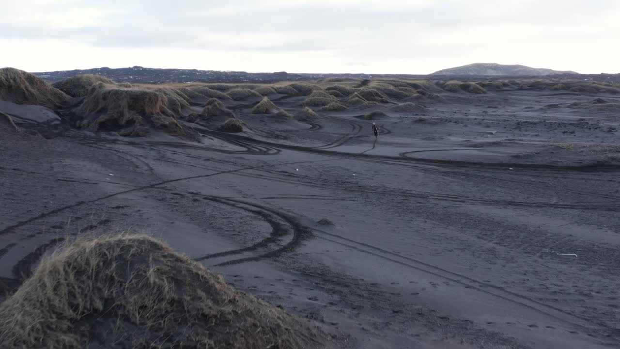 검은 모래 해변의 잔디 언덕을 순항하는 익스트림 오토바이 라이더, 공중