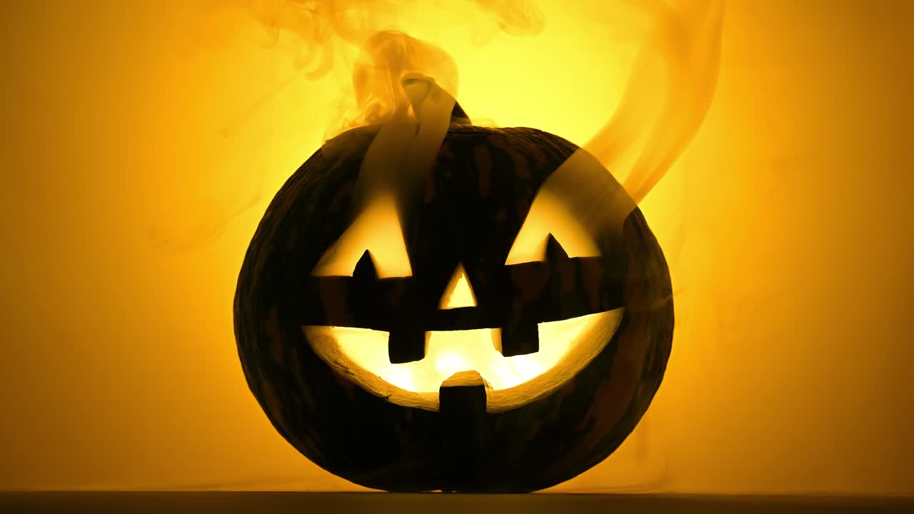divertida linterna de calabaza brillante en el humo sobre un fondo naranja.