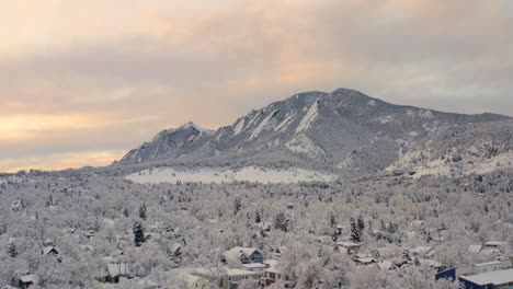 low drone shot moving down of boulder colorado and rocky flatiron mountains after large winter snow storm covers trees, homes, streets, and neighborhood in fresh white snow