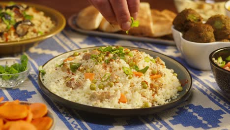 sprinkling greenery on couscous with chicken on table close-up. arabian cuisine. pita and bulgur on background. traditional middle eastern culture. delicious rice with meat. homemade food concept