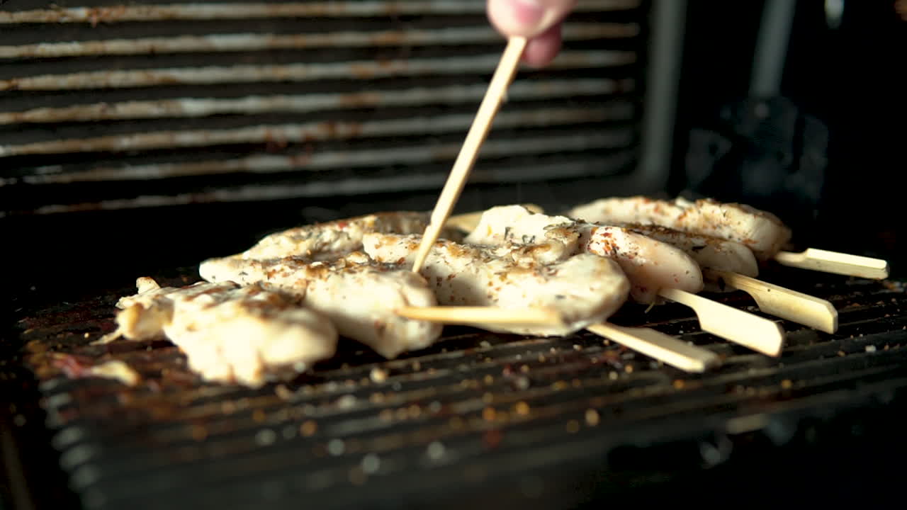 close-up grilled Chicken meat twisted with a wooden stick, the pieces of meat lie spiced on the barbecue, slow motion