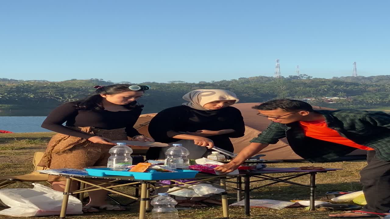 vertical footage, with friends camping and making breakfast of bread, sandwiches, sausages with a view of the clean Sermo reservoir.
