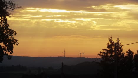 puesta de sol dorada en el área rural con planta de energía eólica visible en las colinas