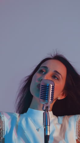 cantante en un vestido blanco sonriendo con las manos en el aire, actuando alegremente en un micrófono vintage. su cabello está fluyendo contra un suave fondo de gradiente de rosa y azul